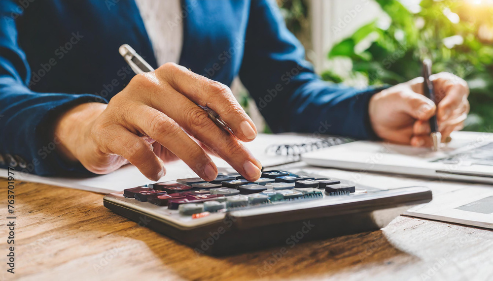 A woman using a calculator at a table, calculating her household expenses and bills. A woman using a calculator at a table, calculating her household expenses and bills.