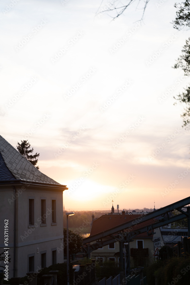A house with a roof and windows is outlined by the setting sun against a backdrop of colorful clouds and sky, with trees in the foreground creating a tranquil dusk landscape A house with a roof and windows is outlined by the setting sun against a backdrop of colorful clouds and sky, with trees in the foreground creating a tranquil dusk landscape