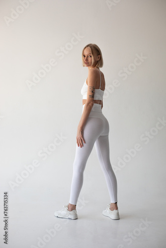 Fototapeta Naklejka Na Ścianę i Meble -  Beautiful blonde girl posing on a white background in white leggings and a white top