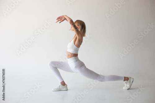 Beautiful blonde girl posing on a white background in white leggings and a white top