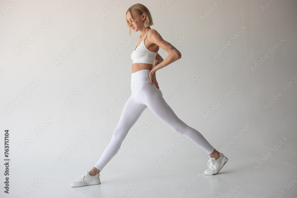 Beautiful blonde girl posing on a white background in white leggings and a white top