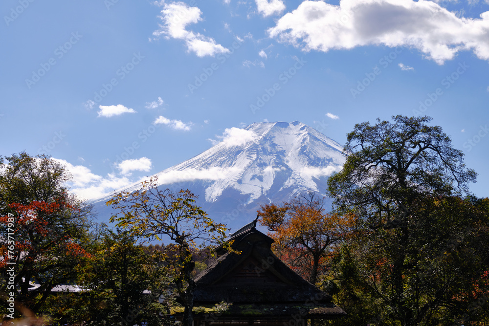 Fototapeta premium Close-up of Mount Fuji seen from Oshino Hakkai village, Yamanashi, Japan. Silhouette of trees and traditional houses in the foreground and snow capped Mt Fuji in the background.