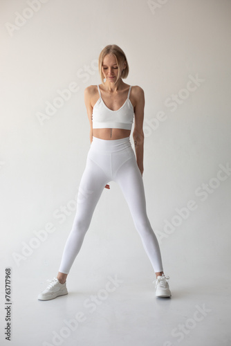 Beautiful blonde girl posing on a white background in white leggings and a white top