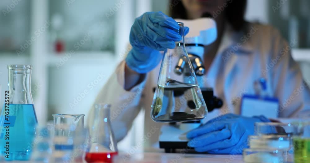 Lab technician stirs liquid in beaker with circular motions Lab technician stirs liquid in beaker with circular motions