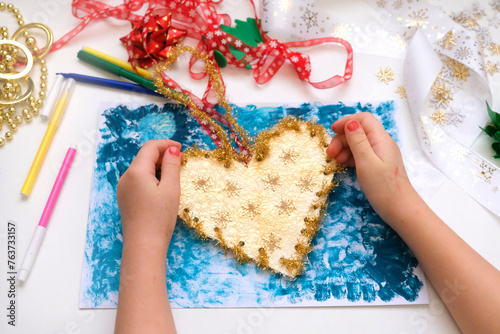 Child making a greeting card, New Year decorations.  Craft for children. Nice greeting card, golden heart. Top view