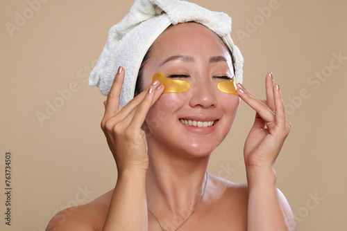 Happy Chinese woman applying undereye patches after shower photo