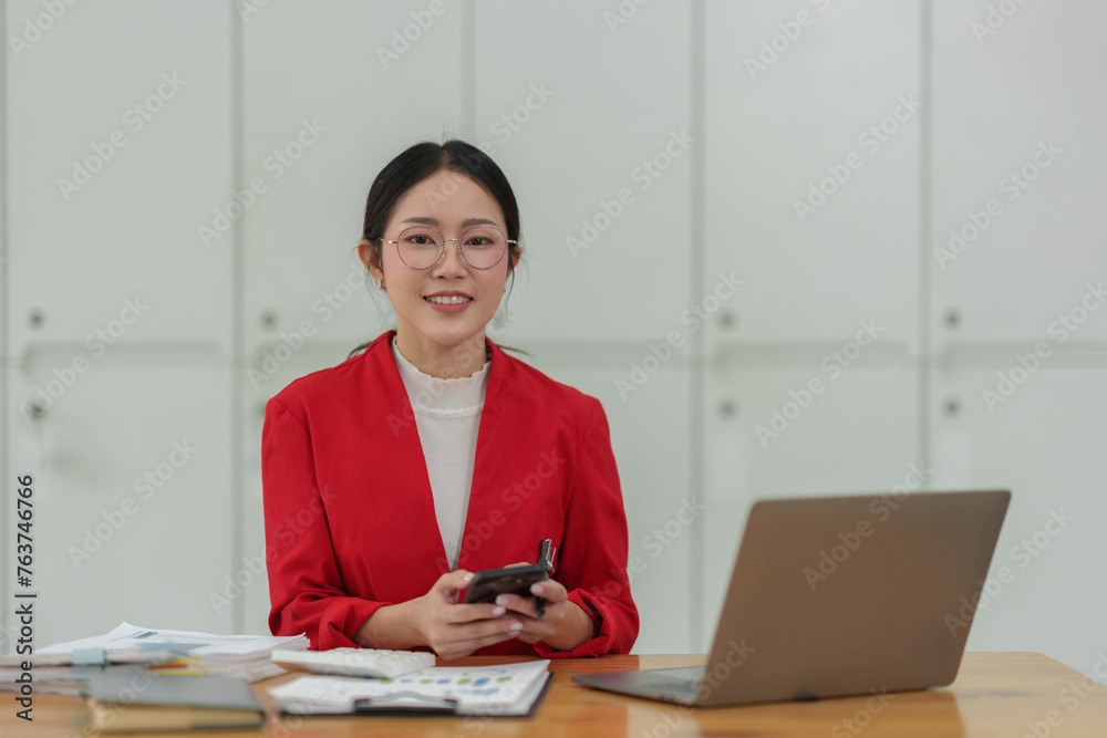 Asian businesswoman wearing glasses in a suit in the office is happy while using a smartphone to contact customers, online, video calls in business finance, marketing, taxes of the company. Asian businesswoman wearing glasses in a suit in the office is happy while using a smartphone to contact customers, online, video calls in business finance, marketing, taxes of the company.