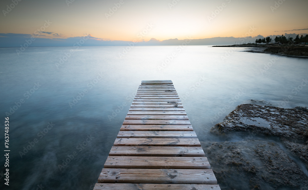 Long wooden pier in the sea at sunrise.