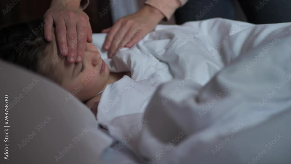 The mothers hands touch the forehead of her 8-year-old daughter, checking the body temperature of the child lying in a bed with white linen. Love and Care of a loving mother for children. The mothers hands touch the forehead of her 8-year-old daughter, checking the body temperature of the child lying in a bed with white linen. Love and Care of a loving mother for children.