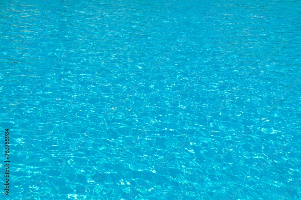 Wide blue swimming pool water background with reflection sunlight. Clear summer water surface texture with ripples, splashes and bubbles. Vacation or travel concept