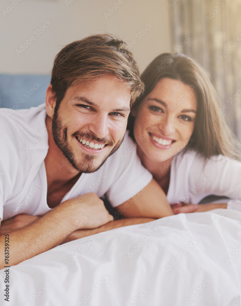 Smile, hotel and portrait of couple on bed for relaxing, bonding and resting together on vacation. Happy, romantic and young man and woman laying in bedroom at modern apartment or home on weekend.