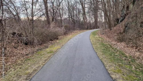 riding a bike on an asphalt bicycle trail (pov view looking down at pavement) passing road, electrical transmission towers in winter with bare trees, green moss, grass biking, cycling view footage photo