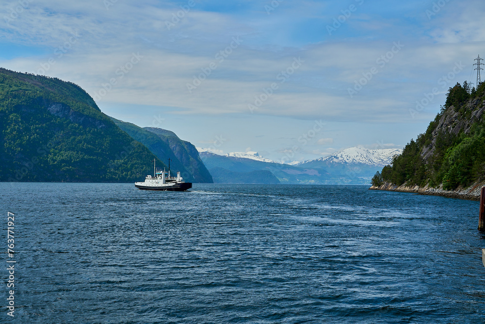 typical norwegian car ferry crossing a beautiful fjord between the mountains transporting passengers and cars on the way to Geiranger on a sunny day,