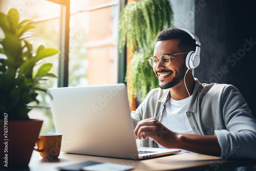 Cheerful Young Man Enjoying Music on Headphones While Working on Laptop in a Cozy Home Office Setting, Exemplifying Remote Work Flexibility and Lifestyle Balance