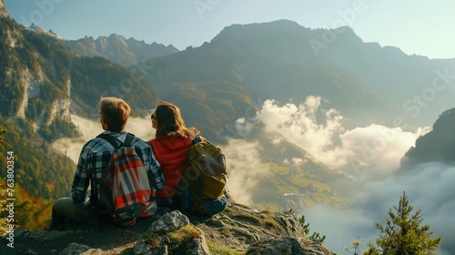 A husband and wife are sitting on the top of a mountain  enjoying nature at sunset.
