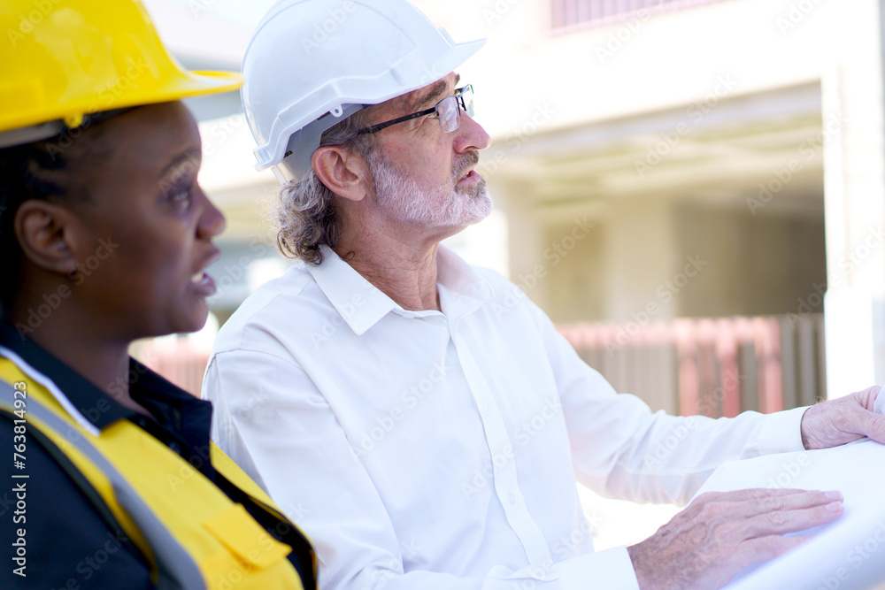 Team of engineer discuss at construction site. Female black ethnicity engineer taking to caucasian white client about the construction plan in blue print. Team of engineer discuss at construction site. Female black ethnicity engineer taking to caucasian white client about the construction plan in blue print.