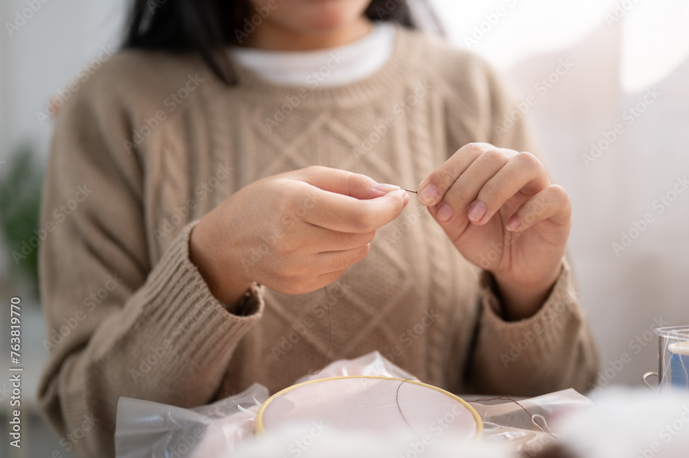 A close-up image of a woman inserting a needle, threading a sewing needle, sewing at home.