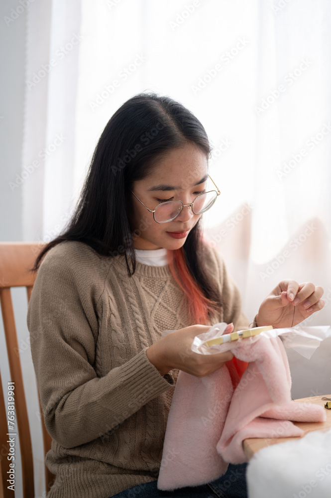 A beautiful Asian woman is focusing on hand-sewing a pattern on cloth on an embroidery frame. A beautiful Asian woman is focusing on hand-sewing a pattern on cloth on an embroidery frame.