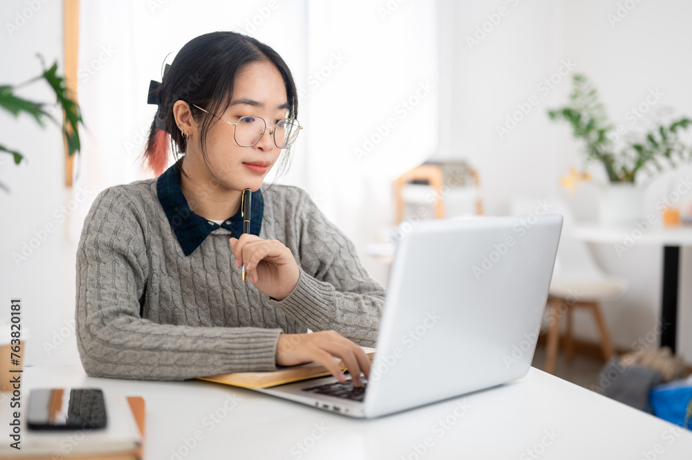 A female college student is focusing on her homework on her laptop in a cafe co-working space.