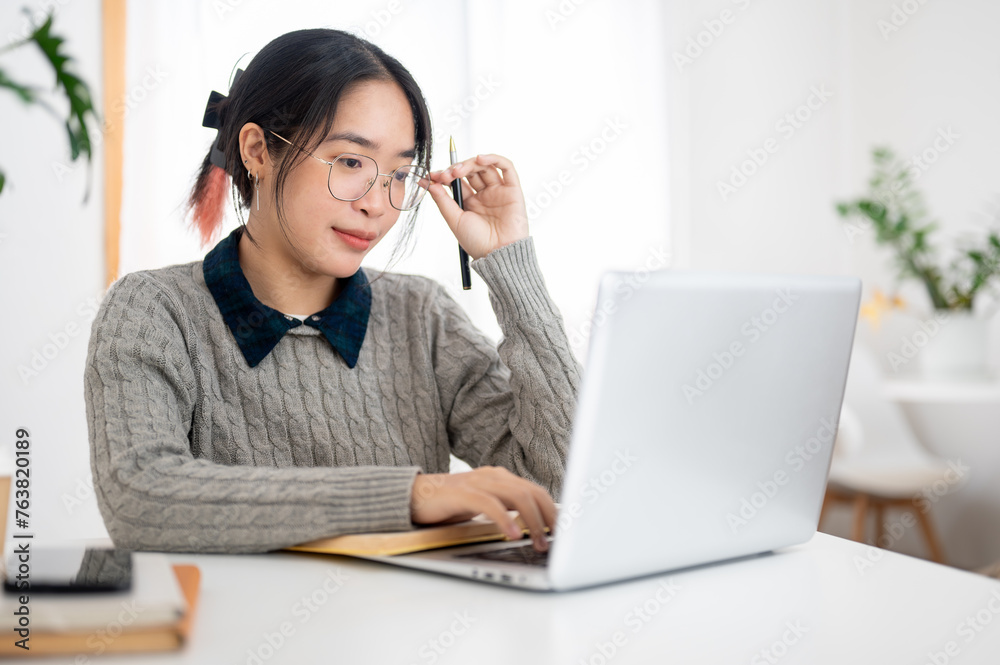 A female college student is focusing on her homework on her laptop in a cafe co-working space. A female college student is focusing on her homework on her laptop in a cafe co-working space.