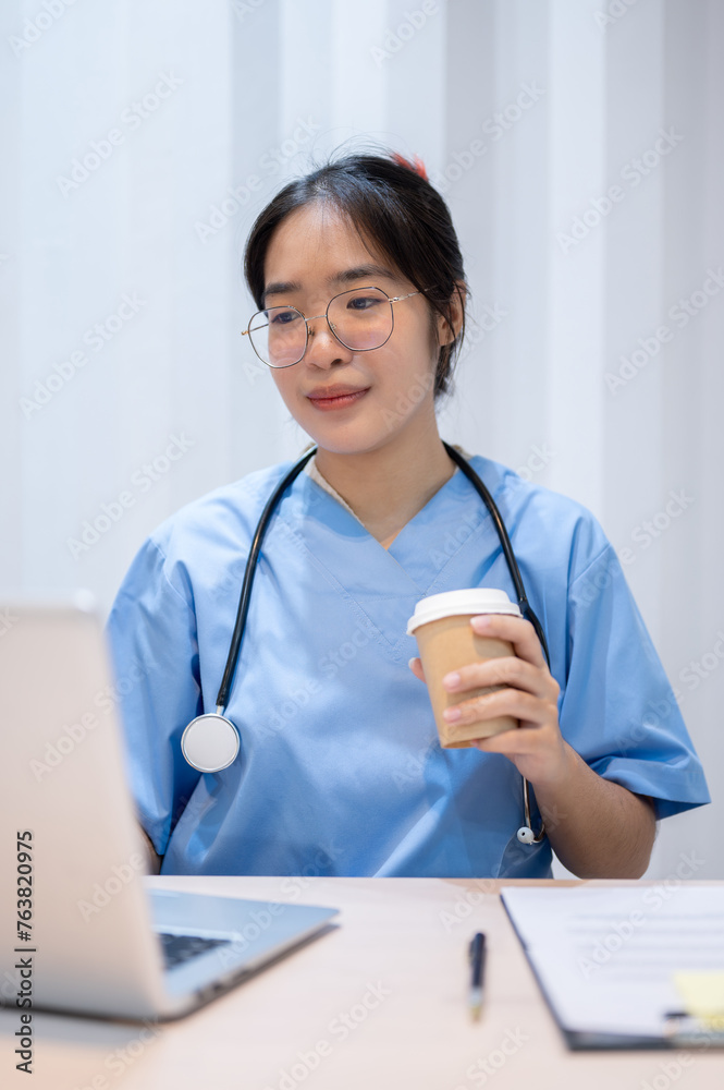 A professional Asian female doctor is sipping coffee while reading medical cases on laptop. A professional Asian female doctor is sipping coffee while reading medical cases on laptop.