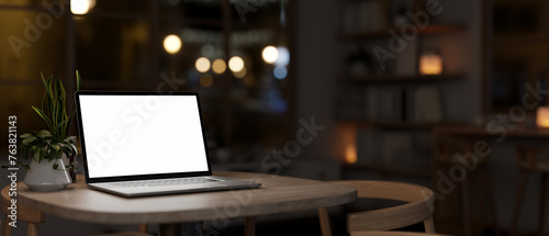 A white-screen laptop computer mockup on a table in a cosy dark living room at night.