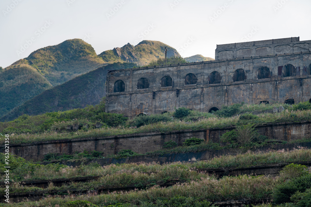 Abandoned mine factory standing on the hill full of grass, in the distance sunlight shines on the peak, in New Taipei City, Taiwan.