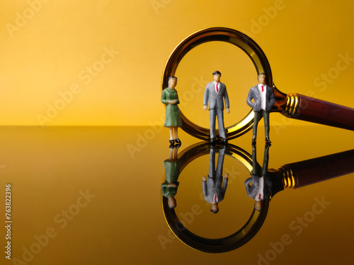 Miniature people and magnifying glass with reflection on a yellow background © Mohd Azrin