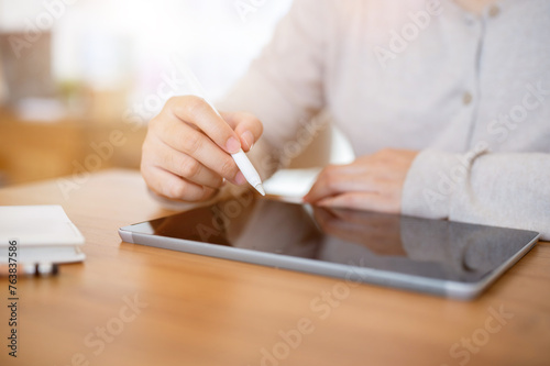 A cropped shot of a woman working on her digital tablet at a table indoors or in a minimalist cafe. © bongkarn