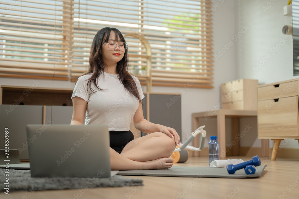 A calm, relaxed young Asian woman in sportswear is meditating on a yoga mat in the living room. A calm, relaxed young Asian woman in sportswear is meditating on a yoga mat in the living room.