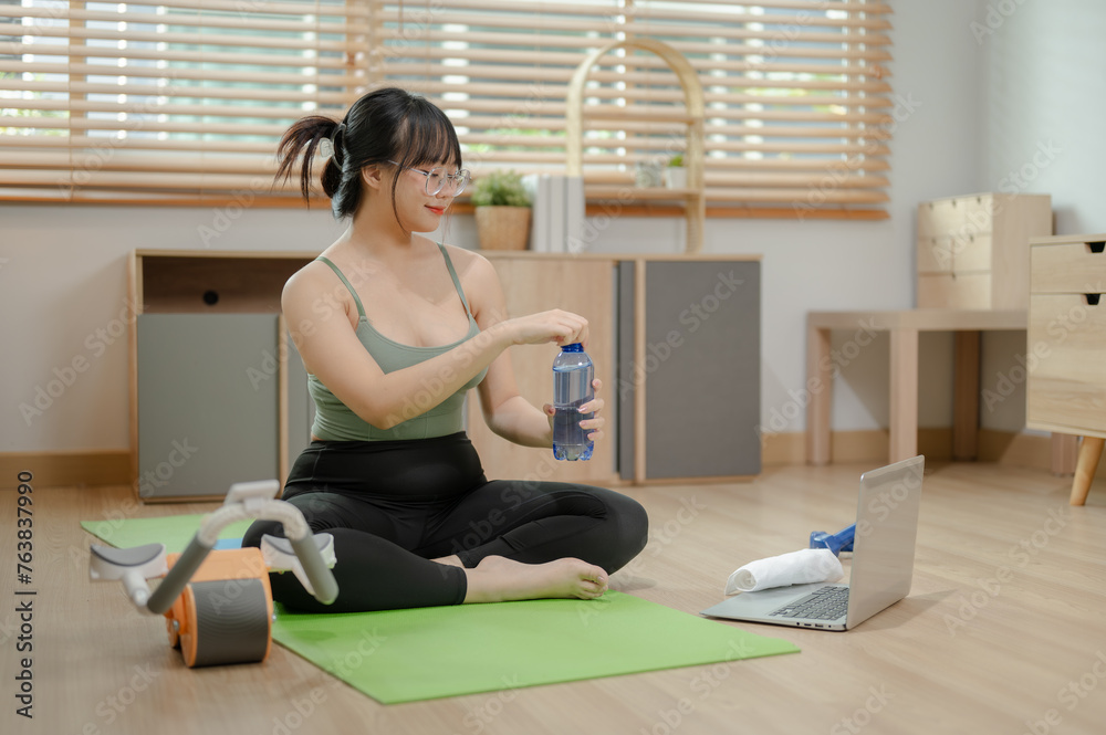 A healthy, fit young Asian woman in sportswear is taking a break after exercise, sipping water. A healthy, fit young Asian woman in sportswear is taking a break after exercise, sipping water.