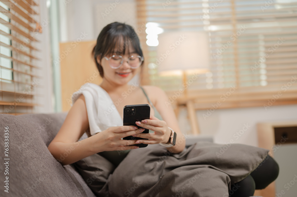A woman is using her phone and relaxing on the sofa in her living room after finishing her workout. A woman is using her phone and relaxing on the sofa in her living room after finishing her workout.