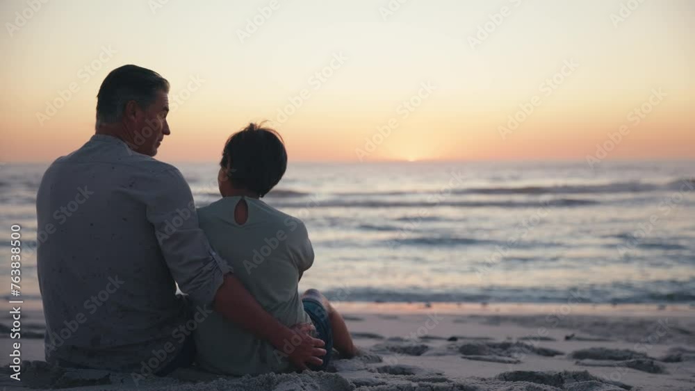 Rear view of mature couple sitting on beach shoreline looking out to sea at sunset - shot in slow motion Rear view of mature couple sitting on beach shoreline looking out to sea at sunset - shot in slow motion