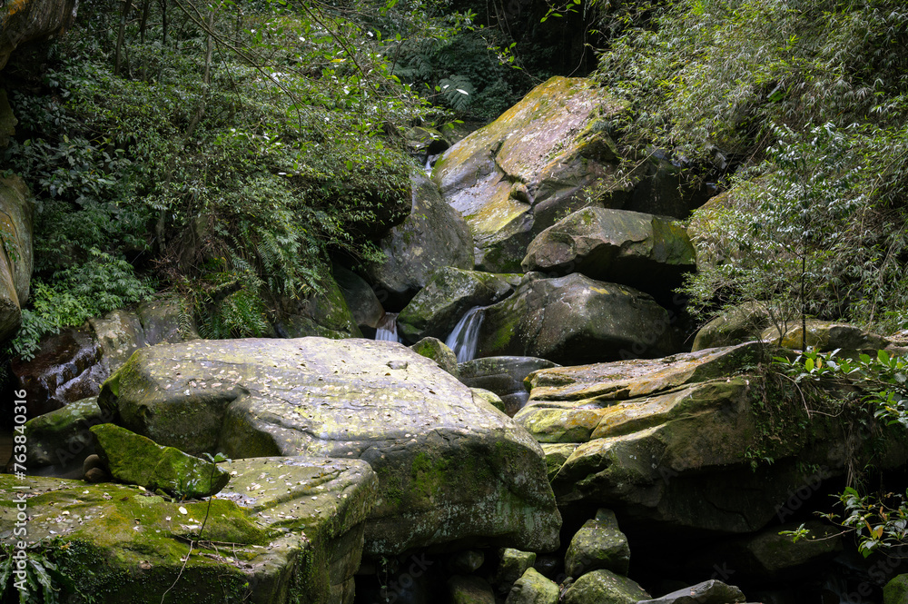 Gorgeous giant rocks full of moss lay on the creek, stream flows gently between the rocks and hidden in the forest, in Nuandong valley, Keelung city, Taiwan.