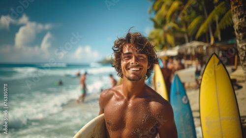 A cheerful, attractive surfer holding his board smiles brightly on a sun-kissed tropical beach with palm trees. © victoriazarubina
