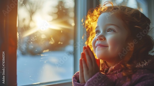 A child gazes out of a frosty window, mesmerized by the golden winter sunrise. The morning light illuminates her face, reflecting her wonder and anticipation.