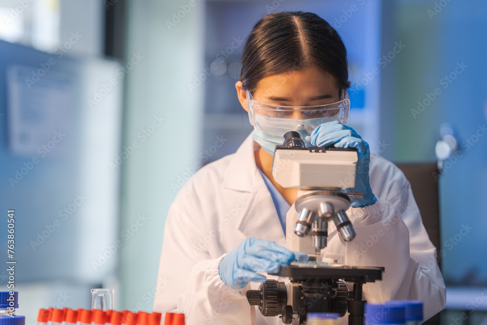Close up female scientist in white lab coat working in biotechnological laboratory, using microscope, pipette, glass flask in clinical laboratory.