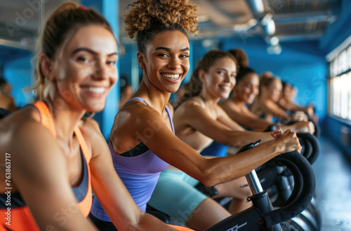 A group of people were riding spinning bikes in the gym, smiling and wearing brightly colored athletic wear like green or blue. They looked focused on their bikes while doing fitness training