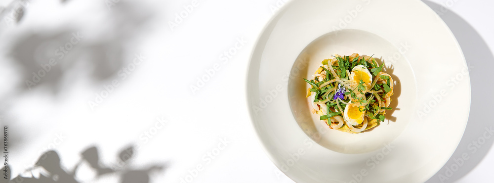 Healthy salad with squid and avocado on white plate with harsh shadows. Calamari salad with vegetables and eggs on white background with shadows of leaves. Summer food menu.