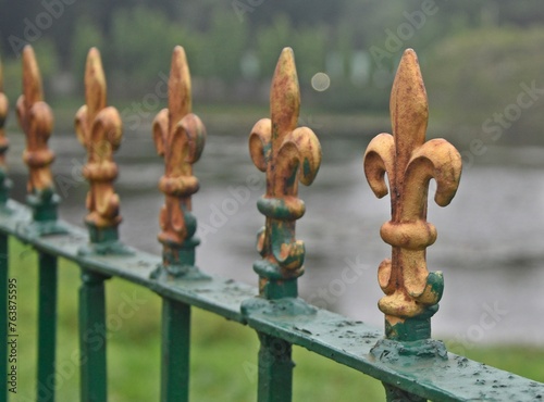 A green fence adorned with fleur-de-lis and featuring a railing spikes design.