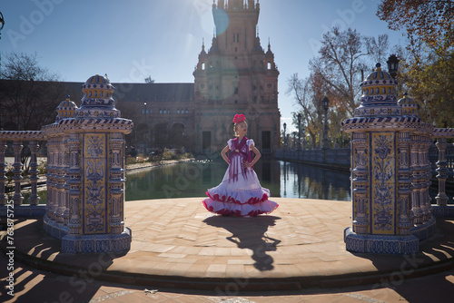 Girl dancing flamenco, posing looking at the camera, in typical flamenco dress, receiving the sun's rays, next to a lake in a beautiful square in Seville. Concept dance, flamenco, typical Spanish.