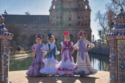Four girls dancing flamenco, posing looking at the camera, in typical flamenco costumes next to a lake in a beautiful square in Seville. Concept dance, flamenco, typical Spanish, Seville, Spain.