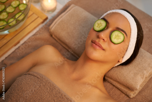 Top view, skincare and woman with cucumber on eyes at massage table in spa for peace, relax or wellness. Mask, above and person with vegetable on face for natural beauty or healthy organic treatment