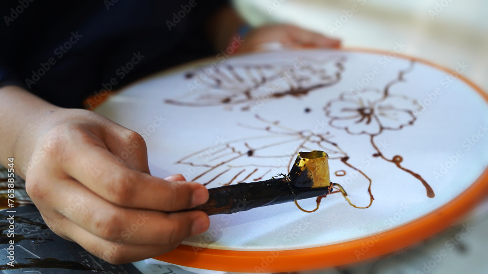 Batik making process, a handmade traditional art from Indonesia. Person carefully trace the butterfly motif on a traditional batik fabric. Produced by technique of wax-resist dyeing applied to fabric.