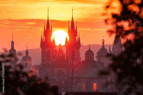 The rising sun in between towers of the Church of Our Lady before Tyn in UNESCO site Prague seen through leaves. photo