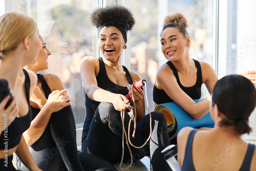 group of happy young interracial women in active wear chatting after workout in pilates studio