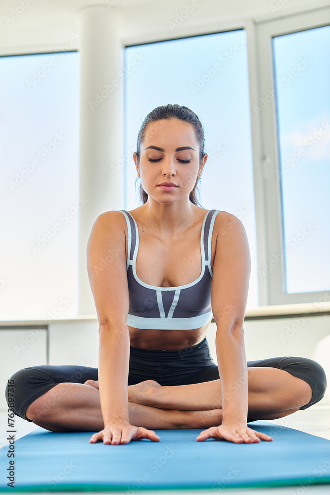 calm and brunette woman in her 20s performing a yoga pose while stretching on a mat in studio calm and brunette woman in her 20s performing a yoga pose while stretching on a mat in studio