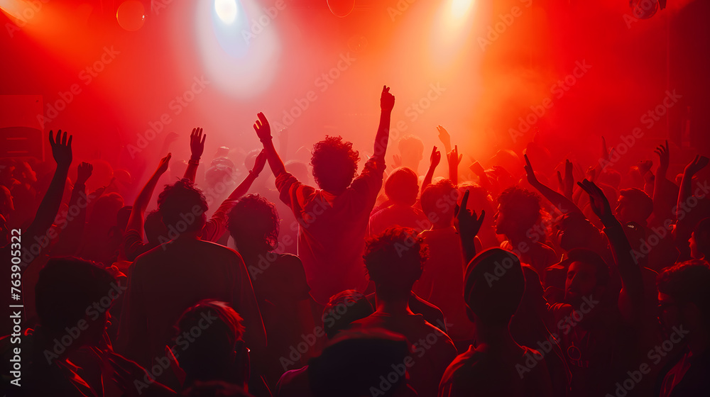 A silhouette of a crowd dancing with hands raised at a music concert with flashing lights