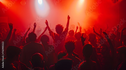 A silhouette of a crowd dancing with hands raised at a music concert with flashing lights