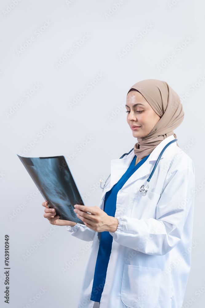 Asian Muslim doctor in hijab and scrubs headphones around her neck Stand confidently in the medical office, isolated on white background, holding x-ray film. Asian Muslim doctor in hijab and scrubs headphones around her neck Stand confidently in the medical office, isolated on white background, holding x-ray film.